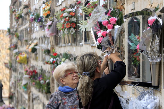 Two women place flowers in front of a family member's niche at Barcelona's Montjuïc cemetery on All Saints' Day (by Laura Fíguls)
